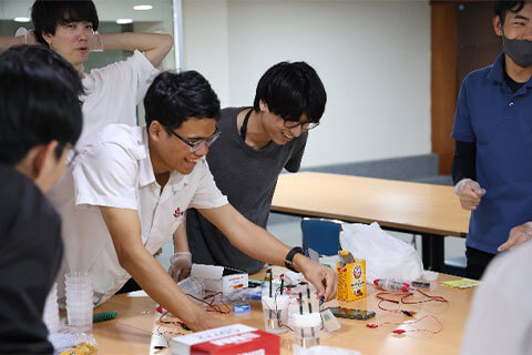 本学とIUHの学生が和やかな雰囲気で協力してイベントの準備を行う(燃料電池の実演)